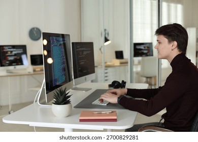 Programmer working on computer with dual monitors at white table in office