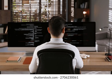 Programmer working on computer with dual monitors at table in office, back view