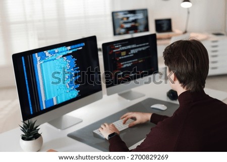 Programmer working on computer with dual monitors at white table in office