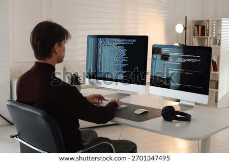 Programmer working on computer with dual monitors at white table in office
