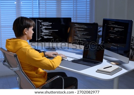 Programmer working on computer with triple monitors and laptop at white table in office