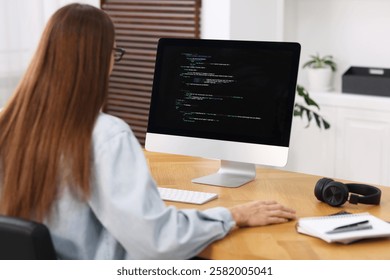 Programmer working on computer at wooden desk indoors, back view