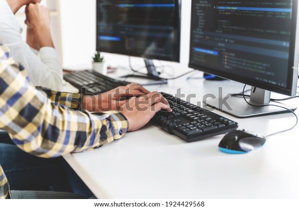 programmer writing program code with two monitors\
and working on new software or hacker programming developing\
software applications in the\
office.