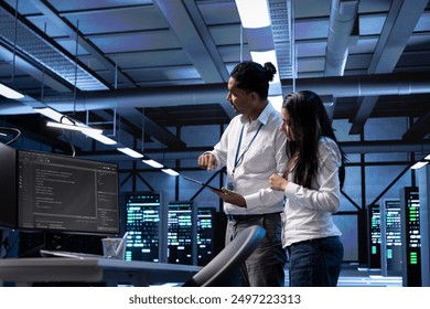 Programmers in data center running system diagnostic tests on PC and tablet to fix problems. IT specialists deploying and error checking utilities on devices to repair network issues in server racks