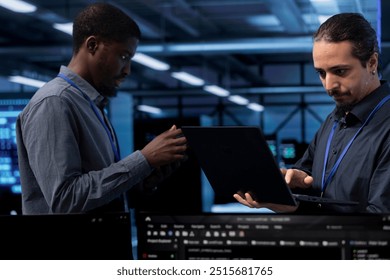 Programmers in data center running system diagnostic tests on laptop to fix problems. Employees deploying and error checking utilities on notebook to fix network issues performance