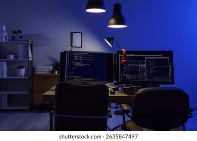 Programmer's desk with computer monitors and glowing lamps in dark office at night