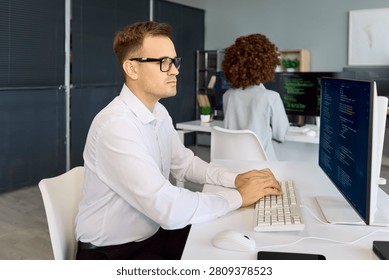Programmers developers coding software teamwork in office. A focused engineer types at a computer with code on a large monitor in a tidy workplace. Strong team focus delivers better code.