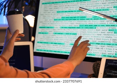 Programmer's hand holding coffee cup while coding on computer screen at night, software development and IT work
