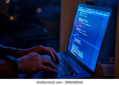 Programmer's hands are coding on a laptop in the dark with a view of the lights of the night city. The concept of a developer or hacker. Saint Petersburg, Russia - 5 July 2021