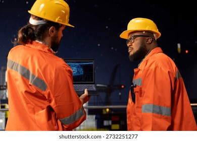 Programmers on offshore oil platform deck using AI to forecast infrastructure maintenance needs. Drilling barge workers use deep learning laptop software to analyze data and prevent mechanical failure