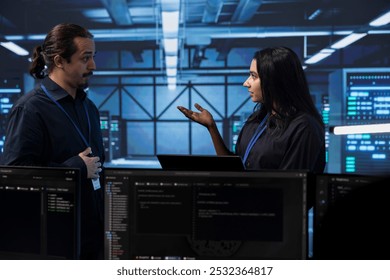 Programmers in server room discussing next steps after checking recovery plan and monitoring energy consumption. Colleagues in data center location talking about routine disk checks results - Powered by Shutterstock