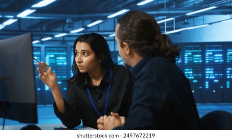 Programmers talking in high tech server hub, using PCs to analyze data. Colleagues examining infrastructure in data center, ensuring system integrity and security, doing brainstorming
