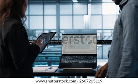 Programmers using AI technology on laptop and tablet in data center employing machine learning models. Devices used by artificial intelligence IT experts in server farm, camera A