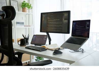 Programmer's workspace with multiple screens and tablet displaying programming code.