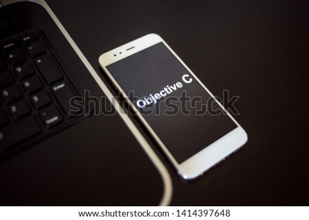 Programming language Objective C for mobile development, concept. Smartphone near the laptop keyboard, the programmer's workplace