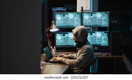 Programming thief breaking through cyber security server and stealing big data on multiple monitors. Hacker with hood using headset and causing computer and system malware with virus. Handheld shot.