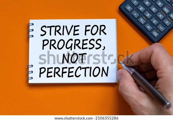 Progress or perfection symbol. Businessman writing
words Strive for progress, not perfection on white note. Black
calculator. Orange background. Business, progress or perfection
concept. Copy space.