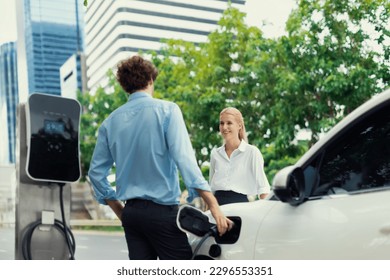 Progressive businessman and businesswoman with electric car parking and connected to public charging station before driving around city center. Eco friendly rechargeable car powered by clean energy. - Powered by Shutterstock