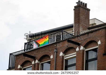 Progressive pride flag displayed on a balcony of a brick building in Amsterdam, Netherlands on 20 July 2025