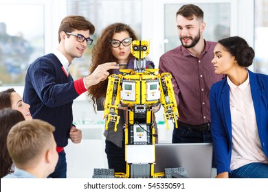 Project Coming To Life. Shot Of A Cheerful Crew Of Young Robot Developers Examining A Robot At Their Office