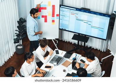 Project manager communicate and collaborate with team using project management software display on monitor, tracking progress of project task and making schedule plan at meeting table. Prudent