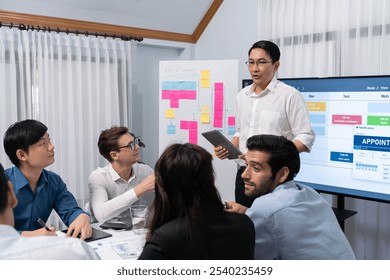 Project manager communicate and collaborate with team using project management software display on monitor, tracking progress of project task and making schedule plan at meeting table. Prudent