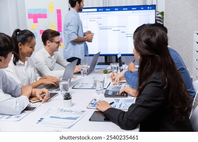 Project manager communicate and collaborate with team using project management software display on monitor, tracking progress of project task and making schedule plan at meeting table. Prudent