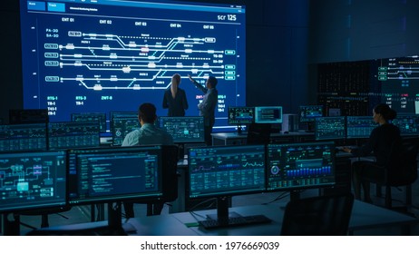 Project Manager and Computer Science Engineer Talking while Using Big Screen Display Showing Infrastructure Infographics and Data.Telecommunications Company System Control and Monitoring Room