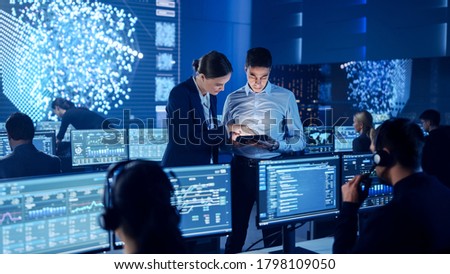 Project Manager and Computer Science Engineer Talking while Using A Digital Tablet Computer. Telecommunications Company System Control and Monitoring Office Room with Working Specialists.