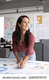 Project manager engaged in planning and analysis, working on business strategy or project development, hold pen, marking or reviewing data charts and graphs laid out on table. Management, strategizing