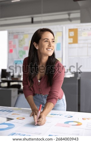 Project manager engaged in planning and analysis, working on business strategy or project development, hold pen, marking or reviewing data charts and graphs laid out on table. Management, strategizing