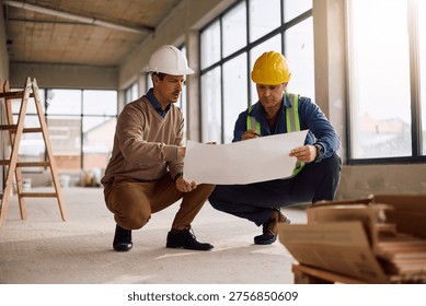 Project manager and worker cooperating while going through rebuilding plans at construction site. 