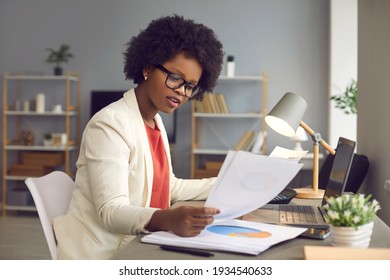 Project Profit Revenue Accounting. Young African American Businesswoman Working With Laptop, Financial Charts And Graphs Reviewing Data In Paper Documents Making Money Work At Office Desk