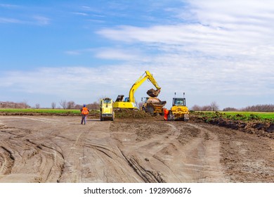Project is in progress, excavator is filling a dumper truck with soil and road roller is flatting, leveling, equates construction site.