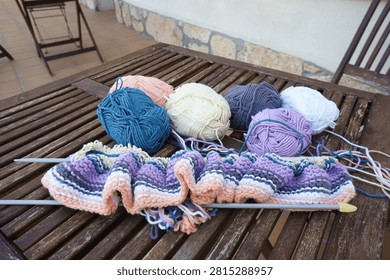 Project in progress with knitting needles and wool making a striped pattern on wood