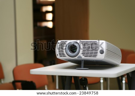 Projector on stand ready for presentation at office with chairs behind in empty hall