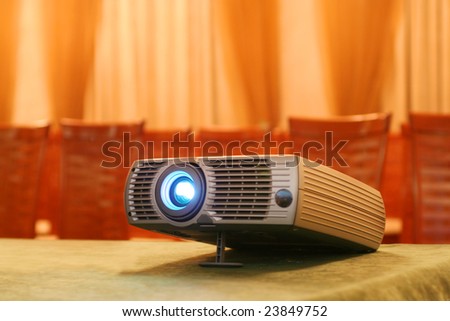 Projector on table with chairs behind in empty hall (horizontal)