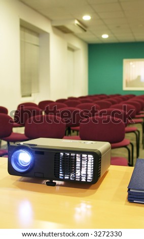Projector on table with chairs behind in empty hall (vertical)