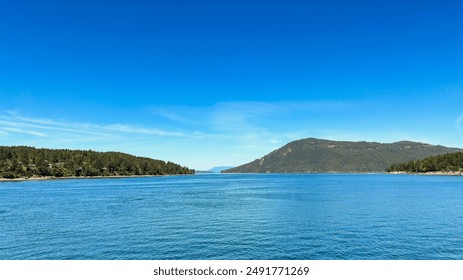 A prominent hill on the right side overlooks calm coastal waters and a clear blue sky. - Powered by Shutterstock