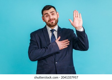 I promise to tell truth! Bearded man wearing official style suit standing raising hand and saying swear, making loyalty oath, pledging allegiance. Indoor studio shot isolated on blue background.