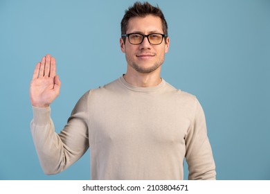 I promise to tell truth. Portrait of honest responsible bearded man standing, raising hand and saying swear, making loyalty oath, pledging allegiance. Indoor studio shot, blue background 