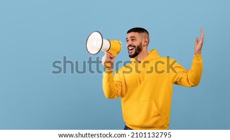 Promo announcement. Happy arab guy with megaphone in hands sharing news or interesting offer over blue studio background, panorama, free space