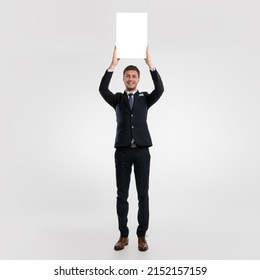 Promotion Billboard Concept. Cheerful Business Man Holding White Advertisement Board In Hands, Standing Isolated On White Studio Background, Raising Lifting Sign Board Up Above Head, Full Body Length