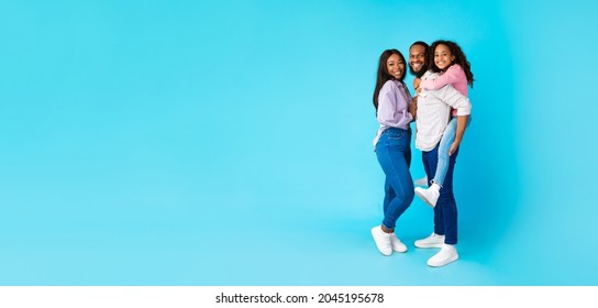 Promotion Concept. Full Body Length Of Funny Black Family Of Three People Posing On Blue Studio Background, Free Copy Space, Panorama, Banner. Cheerful African American Dad Carrying Girl On His Back