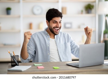 Promotion News. Excited Arab Man Looking At Laptop And Celebrating His Success, Sitting At Home Office Workplace, Raising Fists And Exclaiming With Joy, Emotionally Reacting To Email