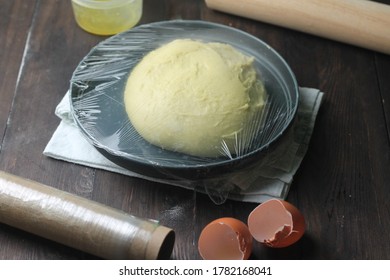 Proofing process of adonan roti or bread or donut dough on grey ceramic bowl, covered with plastic wrap. Rolling pin, egg shell, melted butter glass on wooden dark background. - Powered by Shutterstock