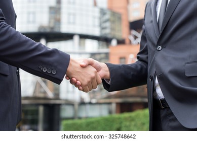 Proper business agreement. Two confident and motivated business  are shaking hands celebrating success. Both men are wearing formal suits. Outdoor business concept - Powered by Shutterstock