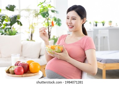 Proper nutrition concept - asian pregnant woman with a fork eating salad