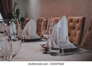 proper serving in restaurant. table covered with a white tablecloth, cutlery and glasses on the table. soft beige chairs. premium restaurant. serving cutlery according to the rules of etiquette.