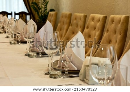 proper serving in restaurant. table covered with white tablecloth, cutlery and glasses on the table. soft beige chairs. Wedding dinner table reception. serving cutlery according to rules of etiquette.